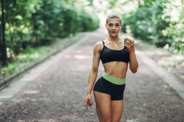 Sportif kadında genç bir siyah spor yeşil elma Açıkhava içinde tutar. Sağlıklı yaşam kavramı.