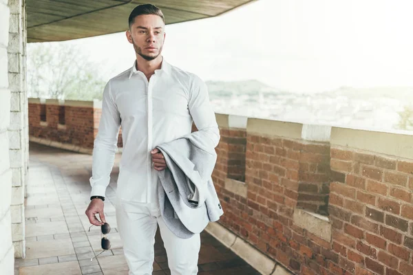 Sakallı ve güneş ışığı altında sokakta şık takım elbise poz içinde gözlüklü genç adam