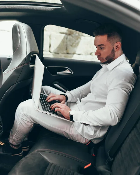 Kendine güvenen genç işadamı arabada otururken diz üstü üzerinde çalışma