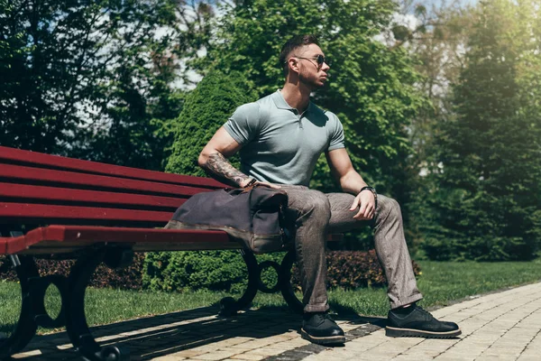 Sakallı ve güneş ışığı altında sokakta şık kıyafet poz içinde gözlüklü genç adam