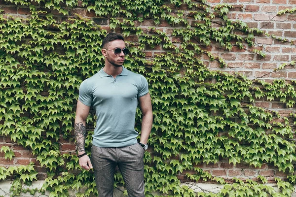 Sakallı ve güneş ışığı altında sokakta şık kıyafet poz içinde gözlüklü genç adam