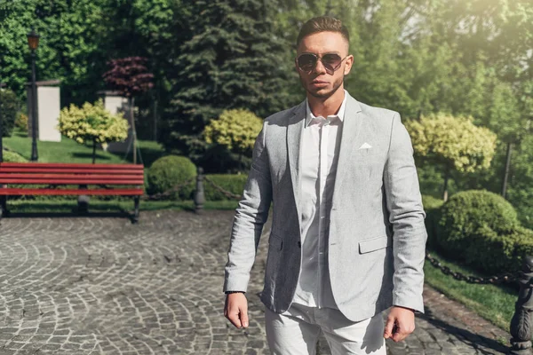 Sakallı ve güneş ışığı altında sokakta şık takım elbise poz içinde gözlüklü genç adam