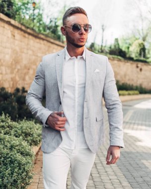 Sakallı ve güneş ışığı altında sokakta şık takım elbise poz içinde gözlüklü genç adam