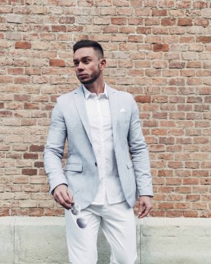 Sakallı ve güneş ışığı altında sokakta şık takım elbise poz içinde gözlüklü genç adam