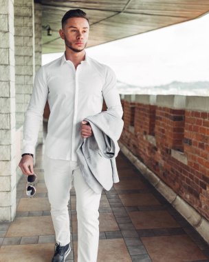 Sakallı ve güneş ışığı altında sokakta şık takım elbise poz içinde gözlüklü genç adam