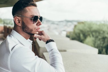 Sakallı ve güneş ışığı altında sokakta şık takım elbise poz içinde gözlüklü genç adam