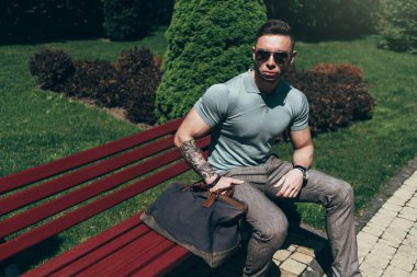 Sakallı ve güneş ışığı altında sokakta şık kıyafet poz içinde gözlüklü genç adam