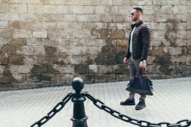 Sakallı ve güneş ışığı altında sokakta şık kıyafet poz içinde gözlüklü genç adam