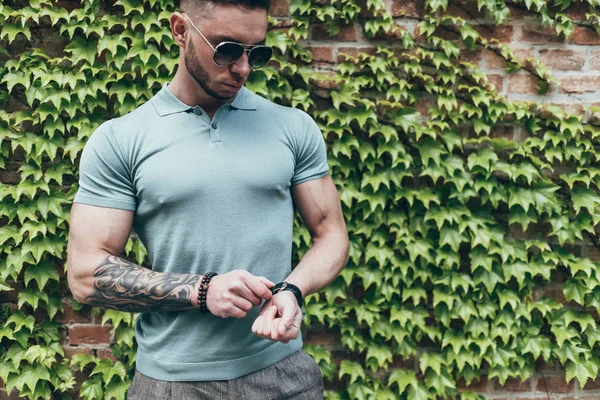 Sakallı ve güneş ışığı altında sokakta şık kıyafet poz içinde gözlüklü genç adam