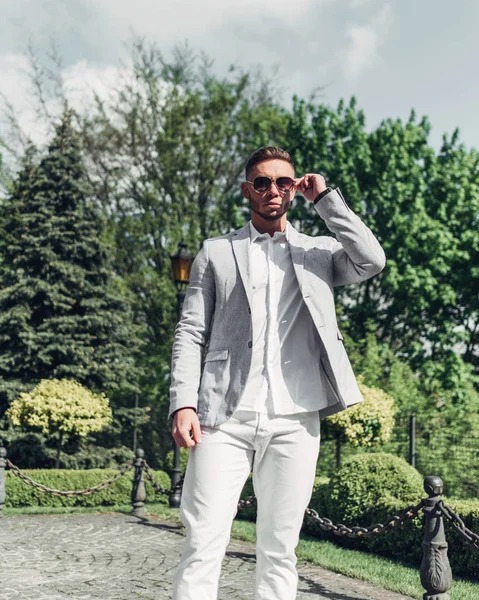 Sakallı ve güneş ışığı altında sokakta şık takım elbise poz içinde gözlüklü genç adam