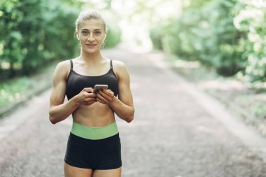 Smartphone cep telefonu ile Bluetooth kulaklık kullanarak müzik dinlemek kadın Runner yaz sabah parkta. Kadın kız dışında yolda koşu.