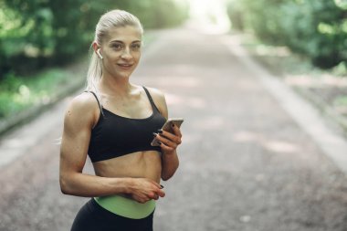 Smartphone cep telefonu ile Bluetooth kulaklık kullanarak müzik dinlemek kadın Runner yaz sabah parkta. Kadın kız dışında yolda koşu.