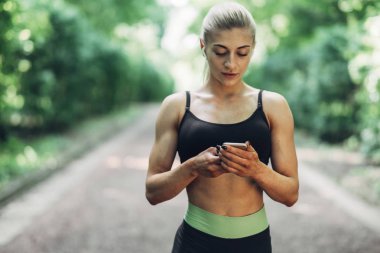 Smartphone cep telefonu ile Bluetooth kulaklık kullanarak müzik dinlemek kadın Runner yaz sabah parkta. Kadın kız dışında yolda koşu.