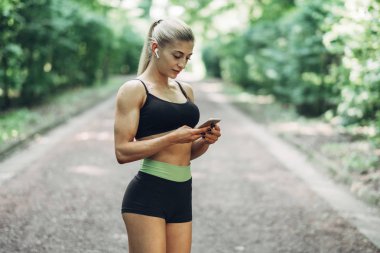 Smartphone cep telefonu ile Bluetooth kulaklık kullanarak müzik dinlemek kadın Runner yaz sabah parkta. Kadın kız dışında yolda koşu.