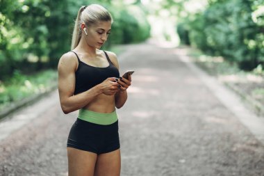 Smartphone cep telefonu ile Bluetooth kulaklık kullanarak müzik dinlemek kadın Runner yaz sabah parkta. Kadın kız dışında yolda koşu.