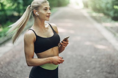 Smartphone cep telefonu ile Bluetooth kulaklık kullanarak müzik dinlemek kadın Runner yaz sabah parkta. Kadın kız dışında yolda koşu.