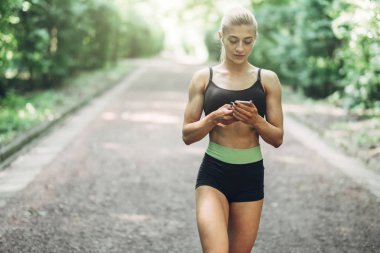 Smartphone cep telefonu ile Bluetooth kulaklık kullanarak müzik dinlemek kadın Runner yaz sabah parkta. Kadın kız dışında yolda koşu.