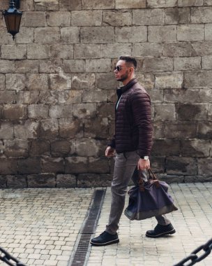 Sakallı ve güneş ışığı altında sokakta şık kıyafet poz içinde gözlüklü genç adam