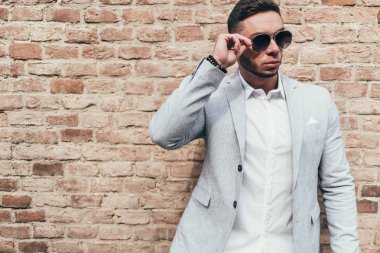 Sakallı ve güneş ışığı altında sokakta şık takım elbise poz içinde gözlüklü genç adam