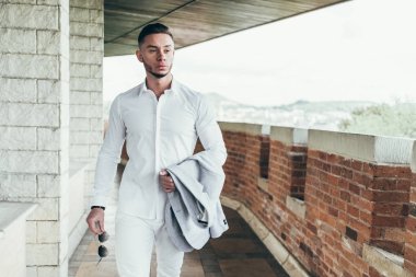 Sakallı ve güneş ışığı altında sokakta şık takım elbise poz içinde gözlüklü genç adam