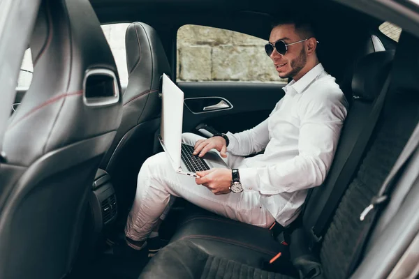 Kendine güvenen genç işadamı arabada otururken diz üstü üzerinde çalışma