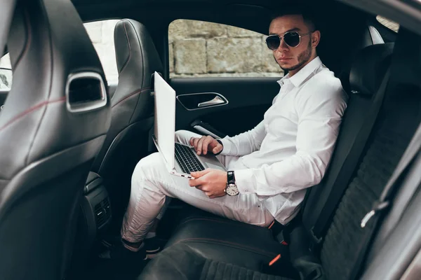 Kendine güvenen genç işadamı arabada otururken diz üstü üzerinde çalışma