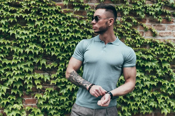 Sakallı ve güneş ışığı altında sokakta şık kıyafet poz içinde gözlüklü genç adam