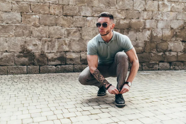 Sakallı ve güneş ışığı altında sokakta şık kıyafet poz içinde gözlüklü genç adam