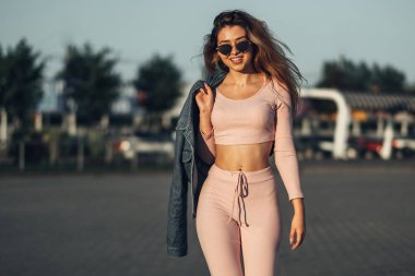 Genç ve güzel kadın sokakta rahat kıyafetler portresi. Pembe gömlek ve pantolon giymiş. Bahar, yaz konsepti. Zaman rahatla. Güneş gözlüklü kız. Şehir Günbatımı keyfini çıkarın.