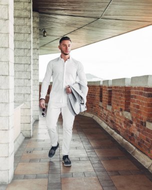 Sakallı ve güneş ışığı altında sokakta şık takım elbise poz içinde gözlüklü genç adam