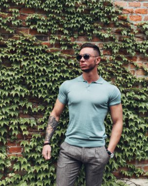 Sakallı ve güneş ışığı altında sokakta şık kıyafet poz içinde gözlüklü genç adam