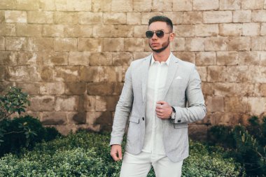 Sakallı ve güneş ışığı altında sokakta şık takım elbise poz içinde gözlüklü genç adam