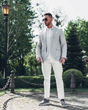 Sakallı ve güneş ışığı altında sokakta şık takım elbise poz içinde gözlüklü genç adam