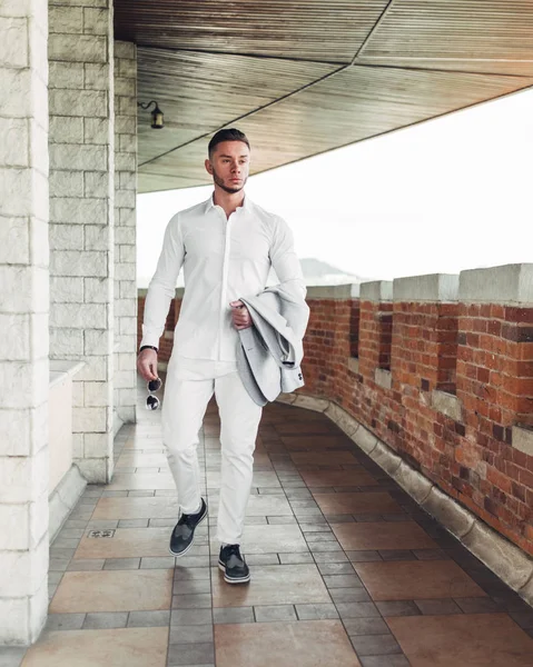 Sakallı ve güneş ışığı altında sokakta şık takım elbise poz içinde gözlüklü genç adam