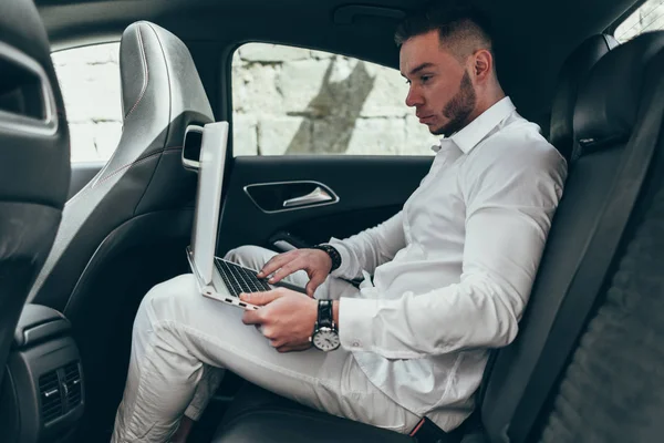 Kendine güvenen genç işadamı arabada otururken diz üstü üzerinde çalışma