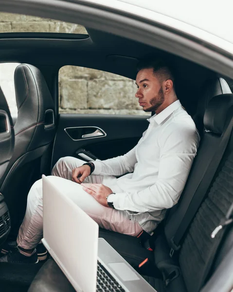 Kendine güvenen genç işadamı arabada otururken diz üstü üzerinde çalışma