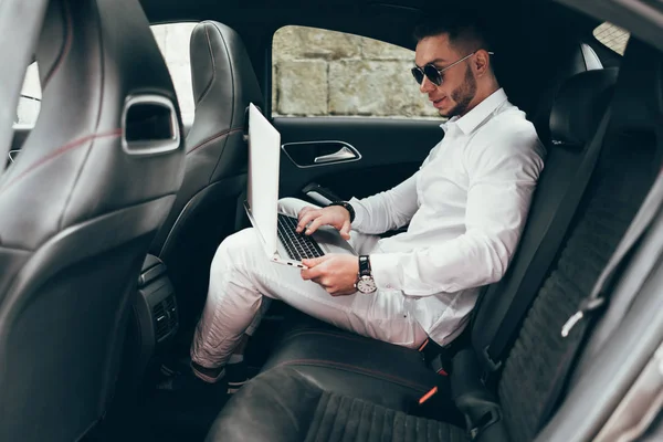 Kendine güvenen genç işadamı arabada otururken diz üstü üzerinde çalışma