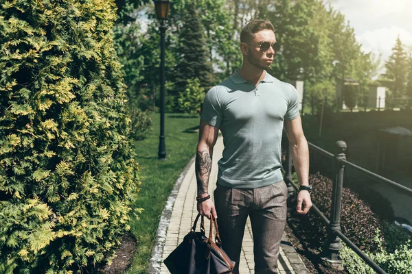 Sakallı ve güneş ışığı altında sokakta şık kıyafet poz içinde gözlüklü genç adam