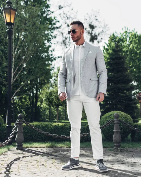 Sakallı ve güneş ışığı altında sokakta şık takım elbise poz içinde gözlüklü genç adam