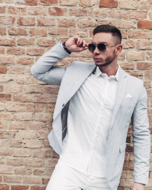 Sakallı ve güneş ışığı altında sokakta şık takım elbise poz içinde gözlüklü genç adam