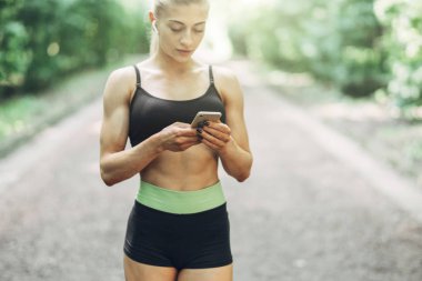 Smartphone cep telefonu ile Bluetooth kulaklık kullanarak müzik dinlemek kadın Runner yaz sabah parkta. Kadın kız dışında yolda koşu.