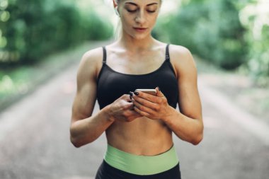 Smartphone cep telefonu ile Bluetooth kulaklık kullanarak müzik dinlemek kadın Runner yaz sabah parkta. Kadın kız dışında yolda koşu.