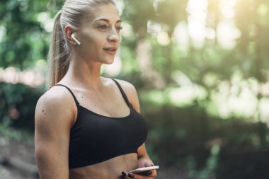 Smartphone cep telefonu ile Bluetooth kulaklık kullanarak müzik dinlemek kadın Runner yaz sabah parkta. Kadın kız dışında yolda koşu.