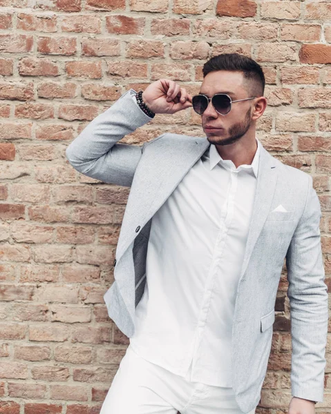 Sakallı ve güneş ışığı altında sokakta şık takım elbise poz içinde gözlüklü genç adam