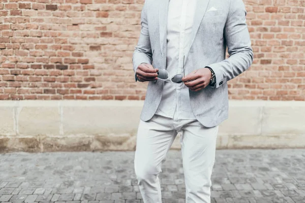 Sakallı ve güneş ışığı altında sokakta şık takım elbise poz içinde gözlüklü genç adam