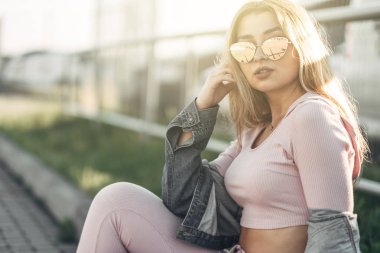Genç ve güzel kadın sokakta rahat kıyafetler portresi. Pembe gömlek ve pantolon giymiş. Bahar, yaz konsepti. Zaman rahatla. Güneş gözlüklü kız. Şehir Günbatımı keyfini çıkarın.