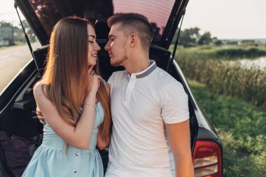Şehir dışında gün batımında arabanın bagajına oturan güzel genç çift