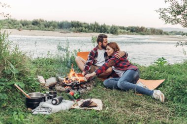 Mutlu genç çift doğa üzerinde piknik şenlik ateşi başına oturmuş