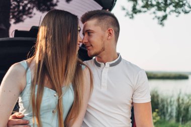 Şehir dışında gün batımında arabanın bagajına oturan güzel genç çift