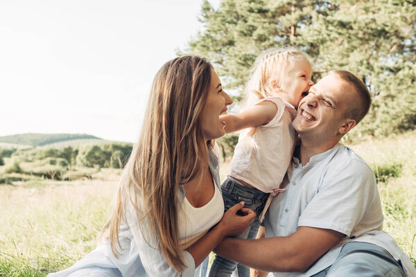 Young Adult Couple with Their Little Daughter Having Fun in the Park Outside the City, Family Weekend Picnic Concept, Three People Enjoying Summer